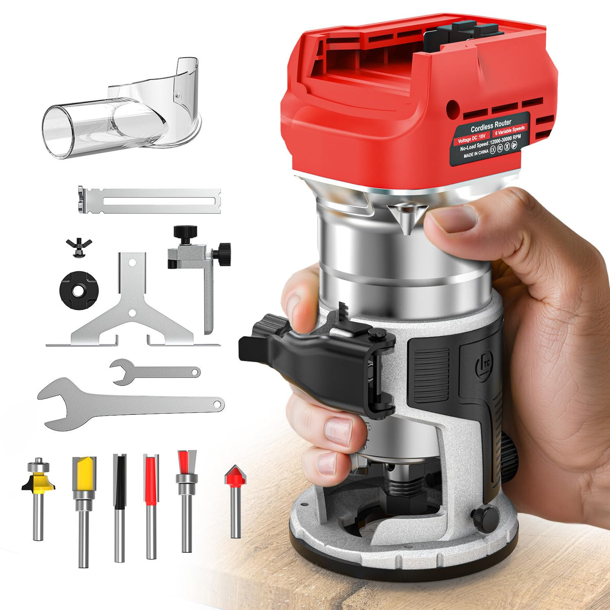 A cordless router with a red and silver body, held by a hand over a light wood surface, with various router bits and accessories arranged on a white background.