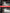 A person in dark work pants carries a black and red portable light with a handle in a warehouse setting. The image includes promotional text reading 'TWO-LEVEL ADJUSTABLE BRIGHTNESS' and brightness callouts showing 50% brightness and 100% brightness.